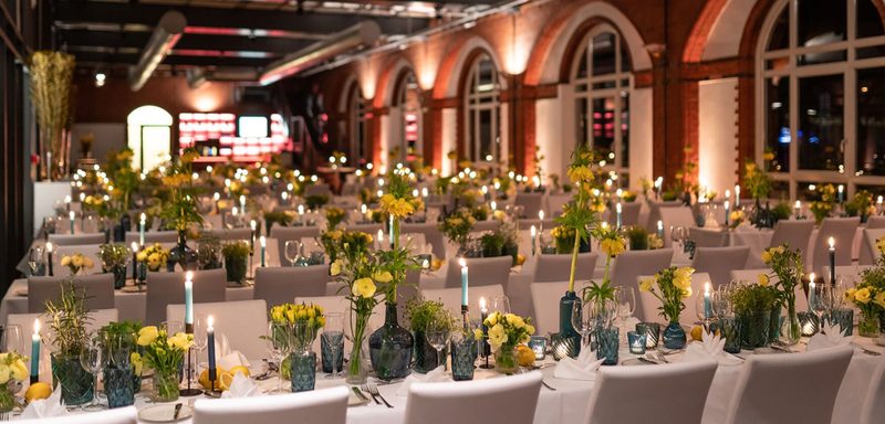 Industrieller Loft mit Backsteinbögen, festlich gedeckten Tischen und Blumendekoration für ein Firmenevent